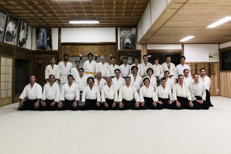 A group photograph inside the Iwama dojo, beneath the portraits on its walls