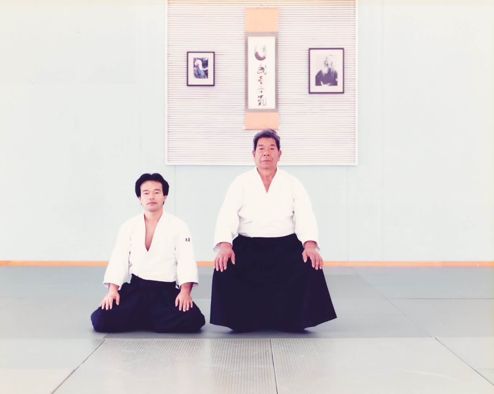 Saburo Takayasu Sensei seated with Morihiro Saito Sensei beneath the Takemusu Aiki scroll
